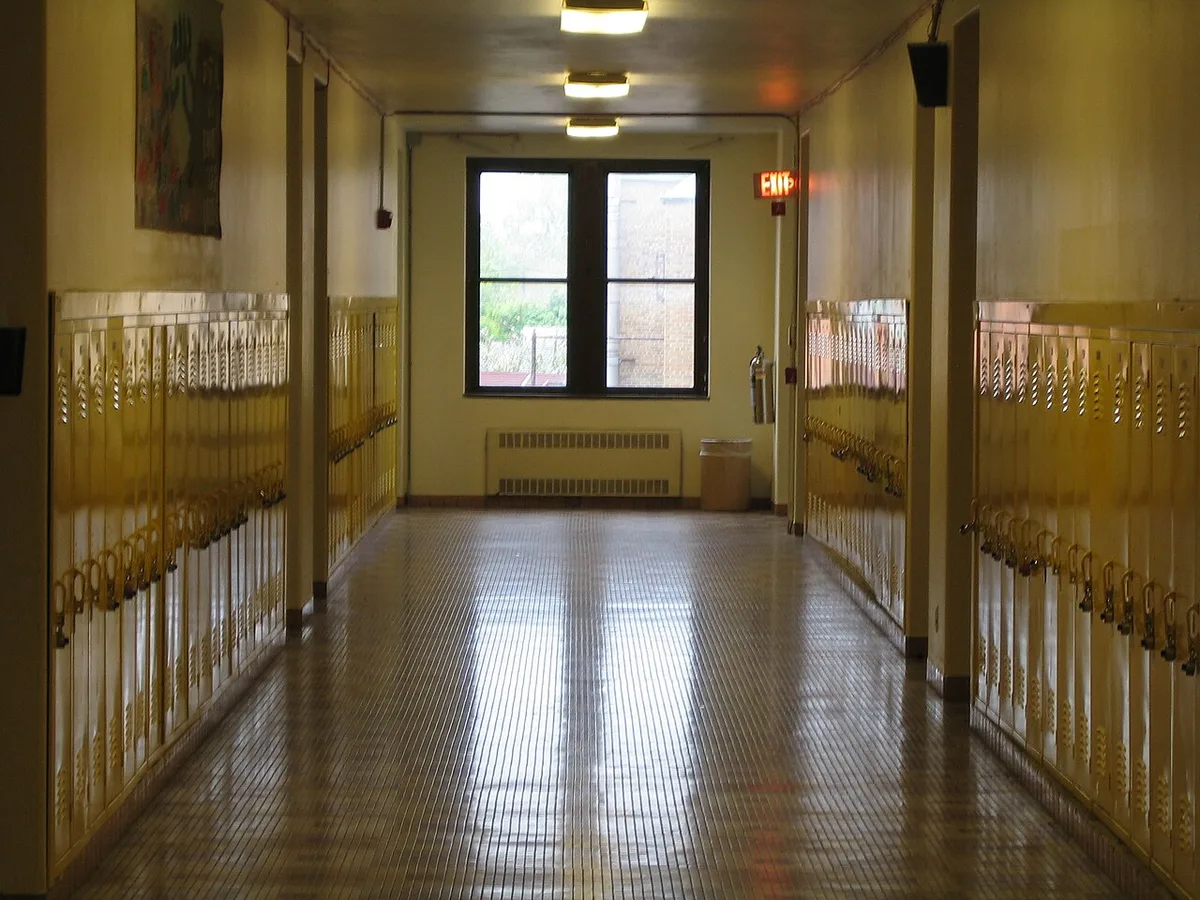 Un couloir de lycée désert bordé de casiers métalliques, éclairé par une fenêtre au fond.