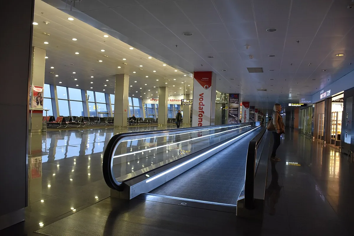 Un tapis roulant vide dans le hall vitré d'un terminal d'aéroport.